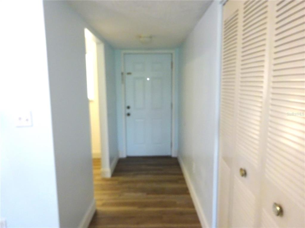 A hallway features light-colored walls, wood-look flooring, a white front door, and a louvered closet door — 2864 N POWERS DRIVE UNIT 156, ORLANDO, FL
