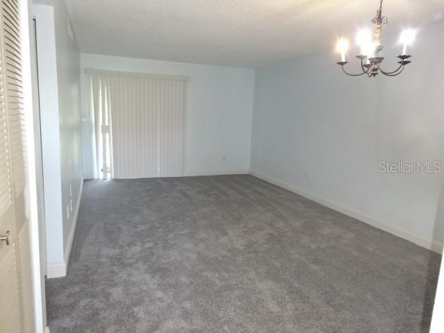 An empty room features gray carpeting, light-colored walls, a chandelier, and sliding glass doors — 2864 N POWERS DRIVE UNIT 156, ORLANDO, FL