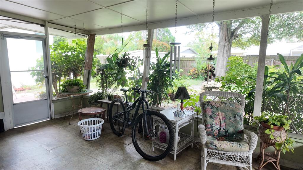 A screened-in porch features tile flooring, a bicycle, a wicker chair, and various potted plants — 7485 17TH STREET N, ST PETERSBURG, FL
