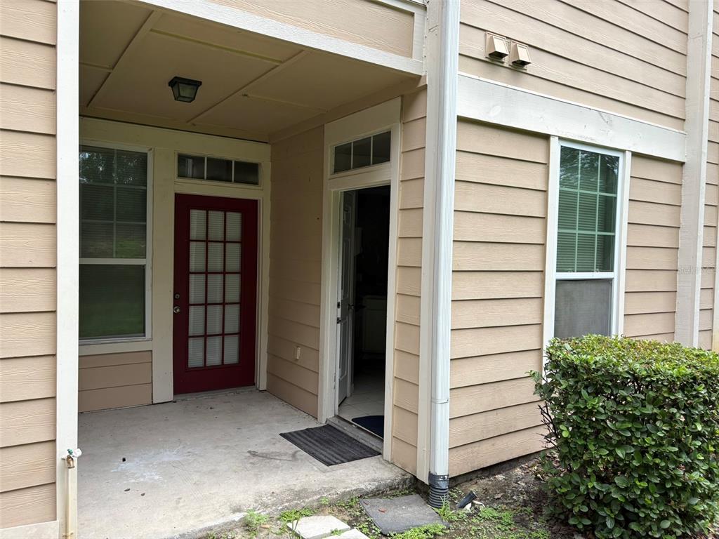 A tan-sided building exterior features a covered concrete patio, a red door, and an entrance — 1101 VINTAGE VILLAGE LANE UNIT 110, OCOEE, FL