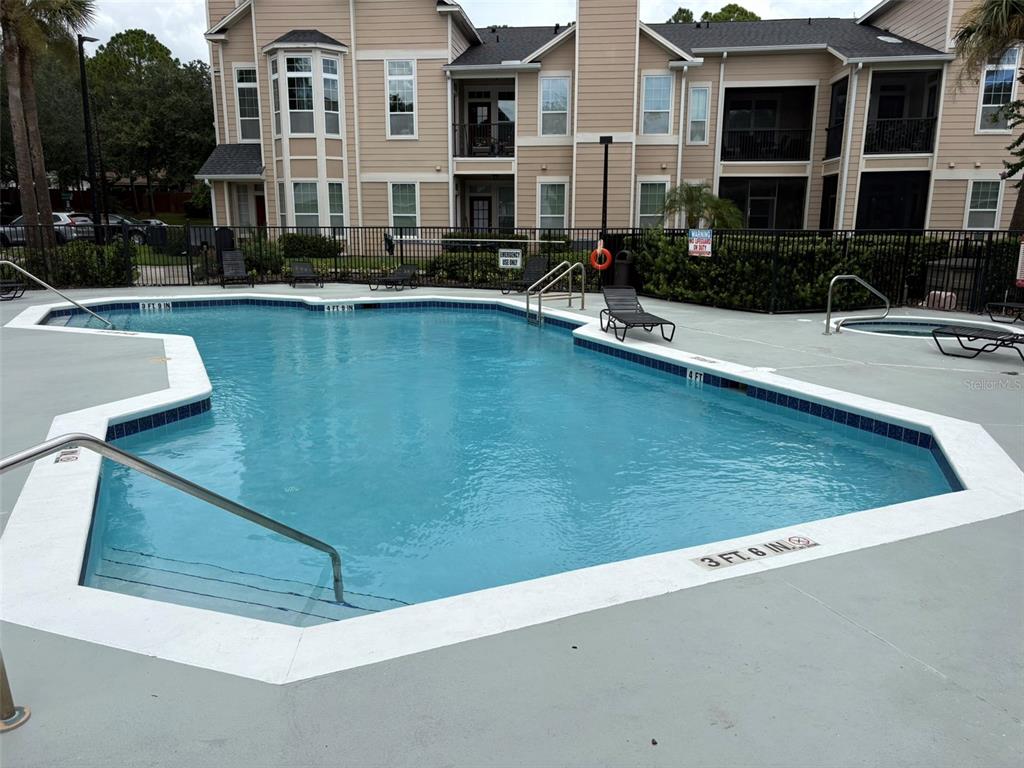 A swimming pool with a metal railing and lounge chairs sits before a tan apartment building — 1101 VINTAGE VILLAGE LANE UNIT 110, OCOEE, FL
