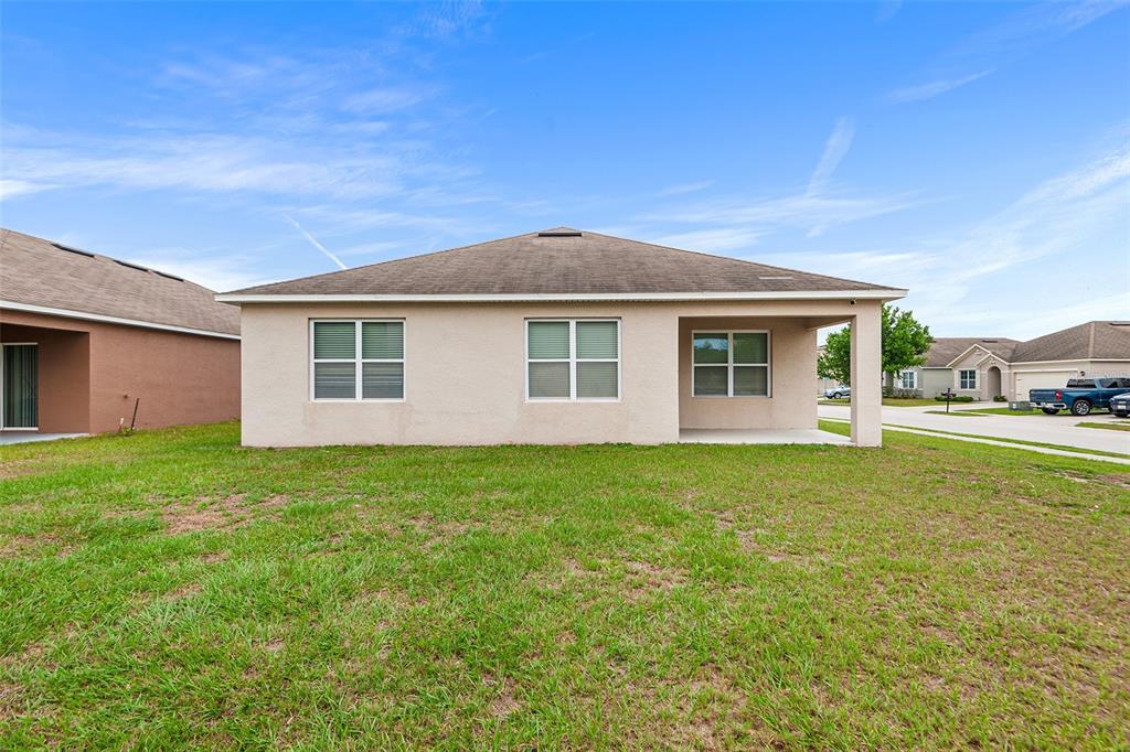 The exterior view shows the rear of a beige stucco house with a covered patio — 4140 SOPHIA BOULEVARD, WINTER HAVEN, FL