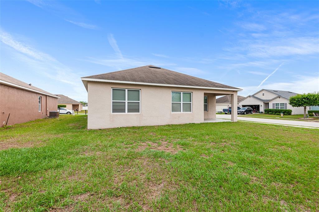 The exterior rear view of a single-story beige house with a covered patio and lawn — 4140 SOPHIA BOULEVARD, WINTER HAVEN, FL