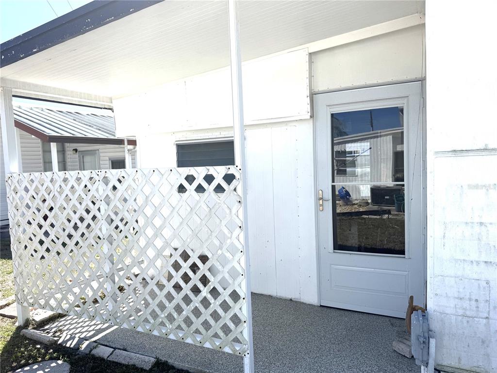 A covered porch features a white lattice privacy screen, a gray door, and concrete flooring — 254 SOUTHWINDS DRIVE, SARASOTA, FL