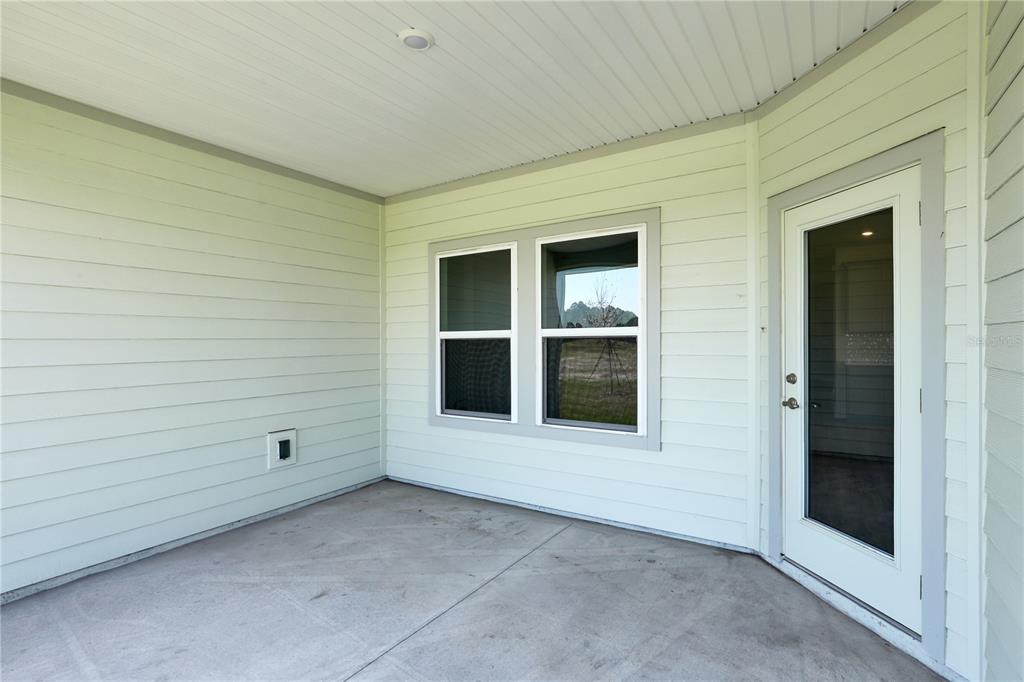 A covered concrete patio features light-colored horizontal siding, a window, and a glass-paneled door — 230 APPLEJACK DRIVE, ST AUGUSTINE, FL