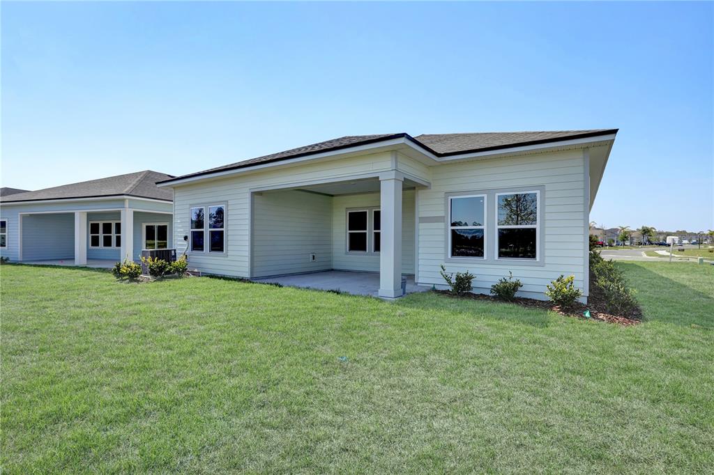 The exterior of a light-colored house features a covered patio and a grassy backyard — 230 APPLEJACK DRIVE, ST AUGUSTINE, FL