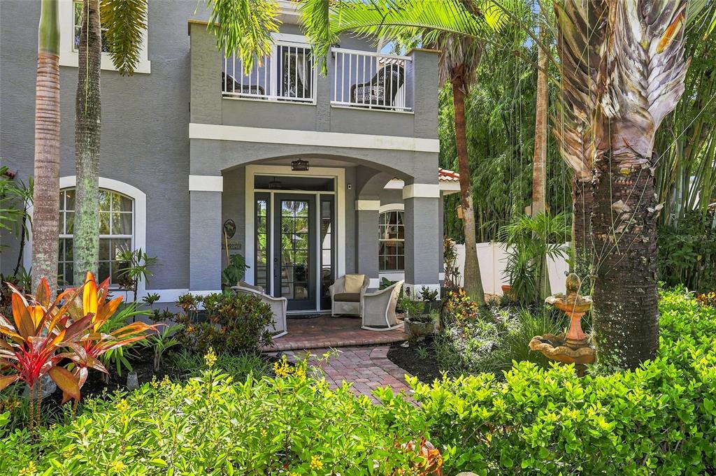 A two-story gray house features a brick walkway, a front porch, and lush tropical landscaping — 5301 ANTHONY LANE, SARASOTA, FL