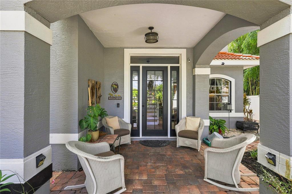 A covered front porch with brick pavers, four wicker chairs, and a glass-paneled front door — 5301 ANTHONY LANE, SARASOTA, FL