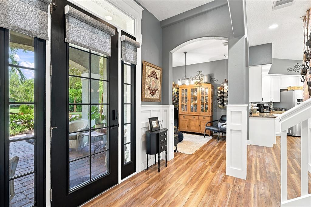 An entryway with wood floors, white wainscoting, and a black door leading to a patio — 5301 ANTHONY LANE, SARASOTA, FL