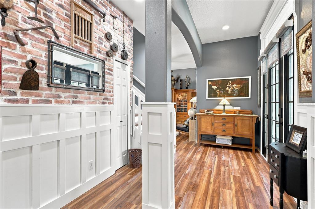 A hallway features a brick wall with vintage decor, white wainscoting, and wood-look flooring — 5301 ANTHONY LANE, SARASOTA, FL