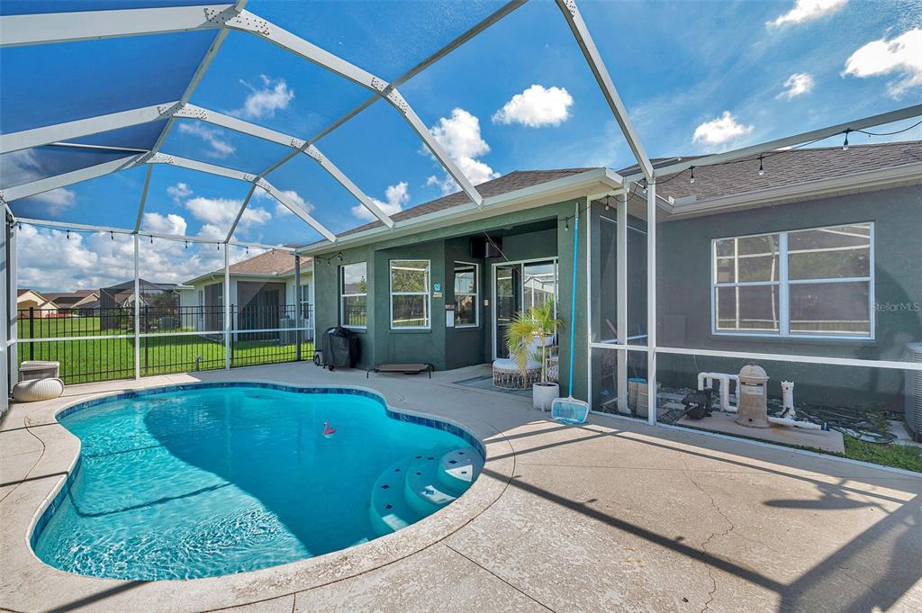 A swimming pool with a screened enclosure sits on a patio behind a house — 4641 ROLLING GREEN DRIVE, WESLEY CHAPEL, FL