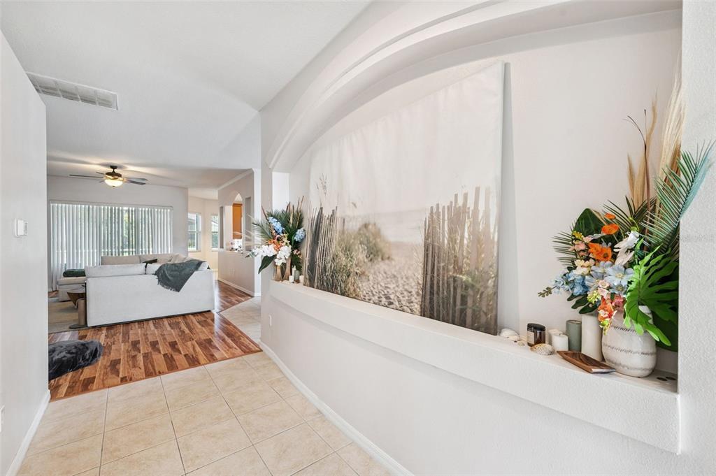 A tiled entryway features a large wall niche displaying a beach-themed canvas and floral arrangements — 4641 ROLLING GREEN DRIVE, WESLEY CHAPEL, FL