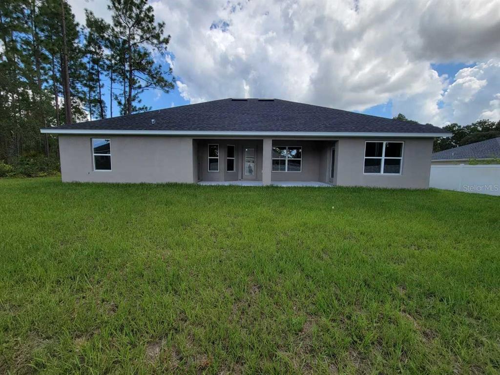 The back exterior of a single-story house features a covered patio and a grassy yard — 16464 SW 54TH COURT ROAD, OCALA, FL