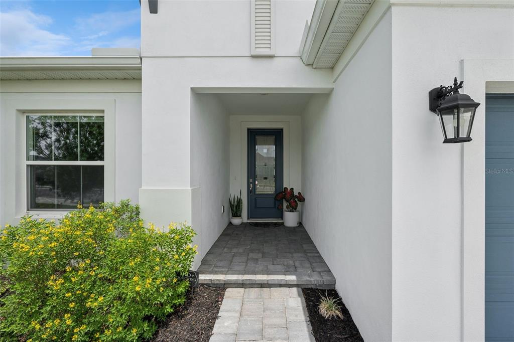 A white exterior home features a blue front door, a paver walkway, and landscaping — 5785 WALLIS LANE, ST CLOUD, FL