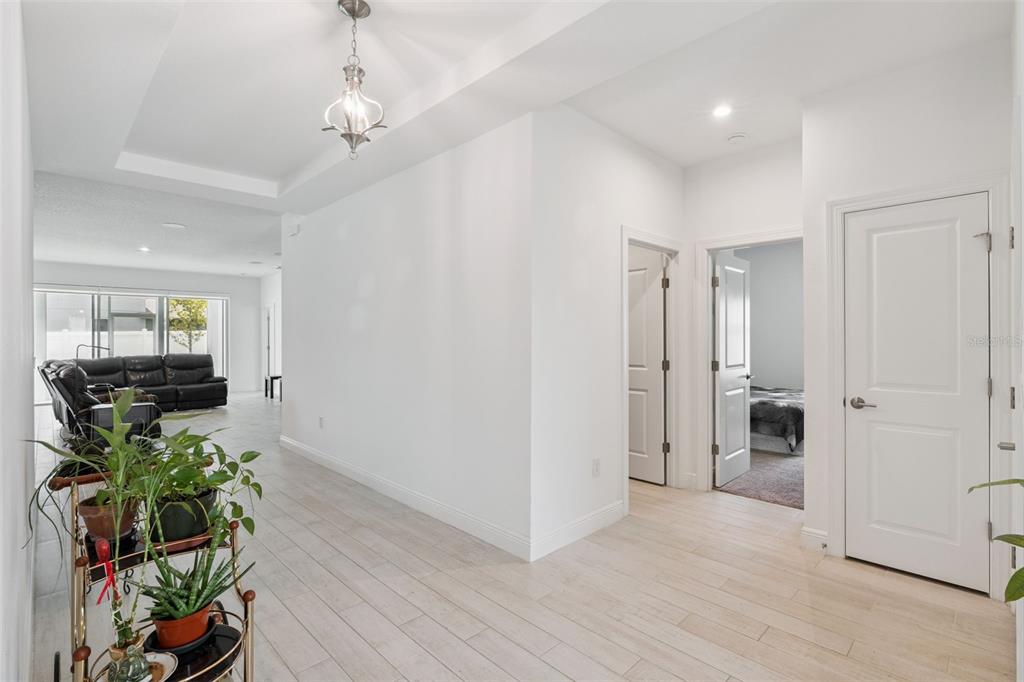 A bright hallway with light wood-look tile floors leads toward a living area with furniture — 5785 WALLIS LANE, ST CLOUD, FL