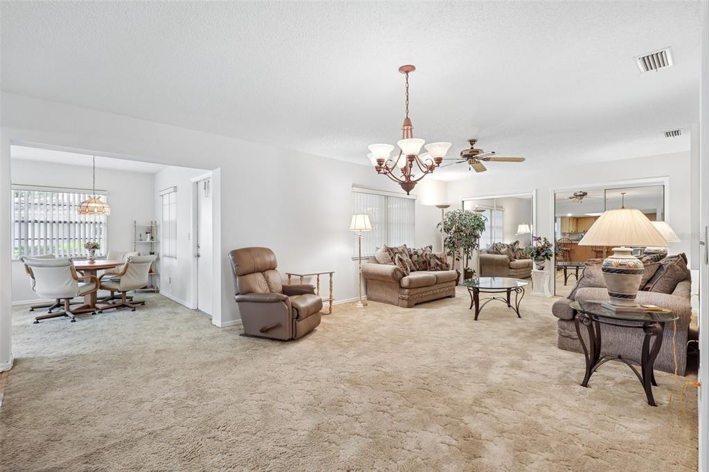 A living room with beige carpeting, a chandelier, and a dining area in the background — 2017 HAMPSTEAD CIRCLE, SUN CITY CENTER, FL
