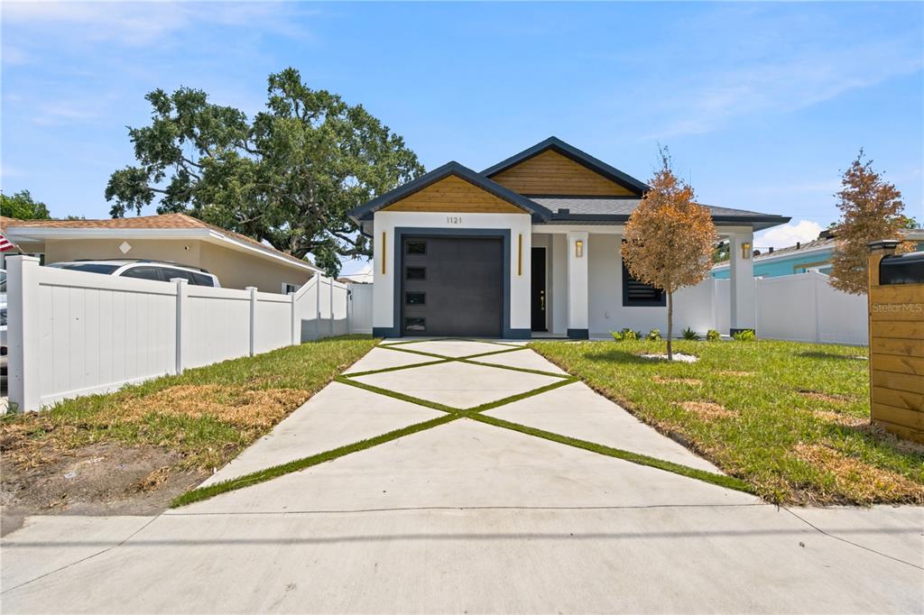 A modern single-story house features a white exterior, a dark garage door, and a patterned driveway — 1121 ENGMAN STREET, CLEARWATER, FL