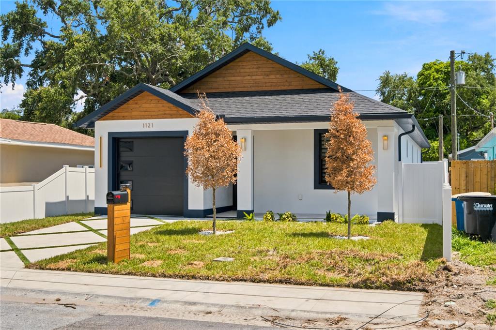 A modern single-story house with a white exterior, wood accents, and a black garage door — 1121 ENGMAN STREET, CLEARWATER, FL