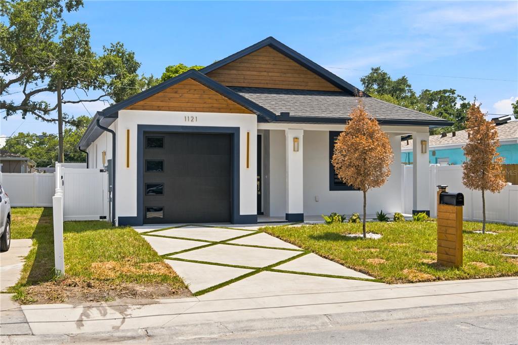 A modern single-story house with a white exterior, dark garage door, and wood-paneled gable — 1121 ENGMAN STREET, CLEARWATER, FL