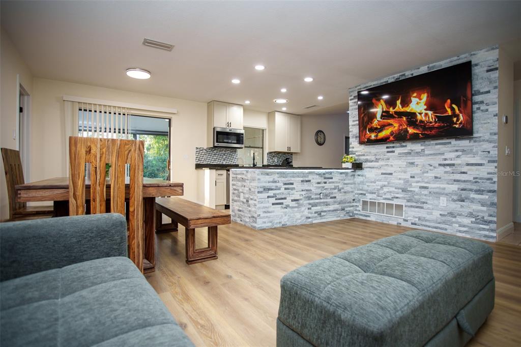 A living room and kitchen area featuring a stone fireplace wall and wood-look flooring — 2719 FOREST KNOLL DRIVE, SARASOTA, FL