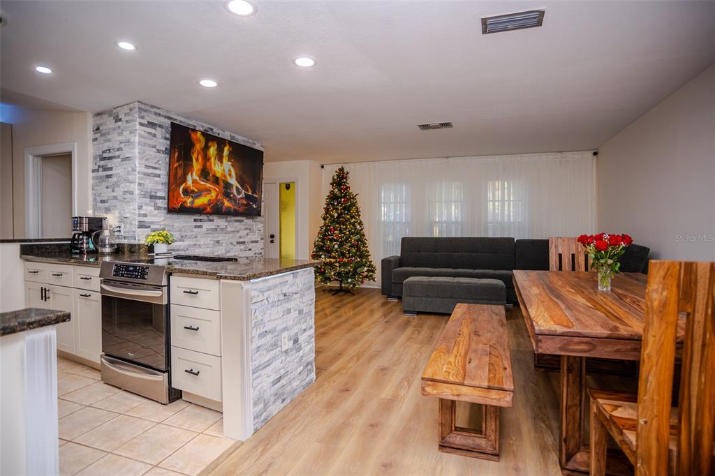 An open-concept kitchen and dining area features a stone-accented island, wood flooring, and a fireplace — 2719 FOREST KNOLL DRIVE, SARASOTA, FL