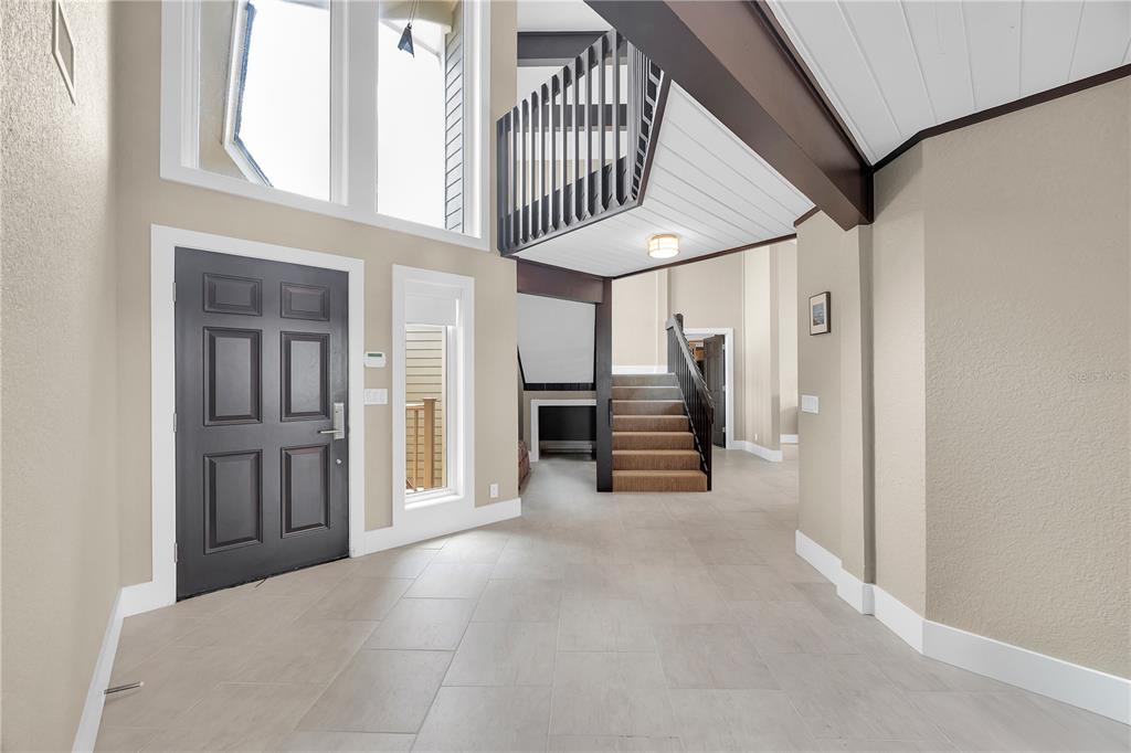 A high-ceilinged foyer features a dark front door, tiled floors, and a wooden staircase — 9353 OLD A1A, ST AUGUSTINE, FL