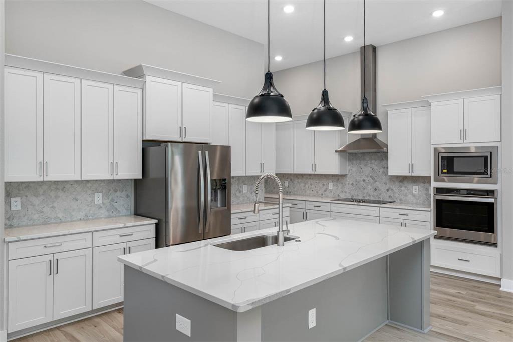 A modern kitchen features white cabinetry, a gray island with a quartz countertop, and stainless appliances — 13063 OLDENBURG DRIVE, HUDSON, FL
