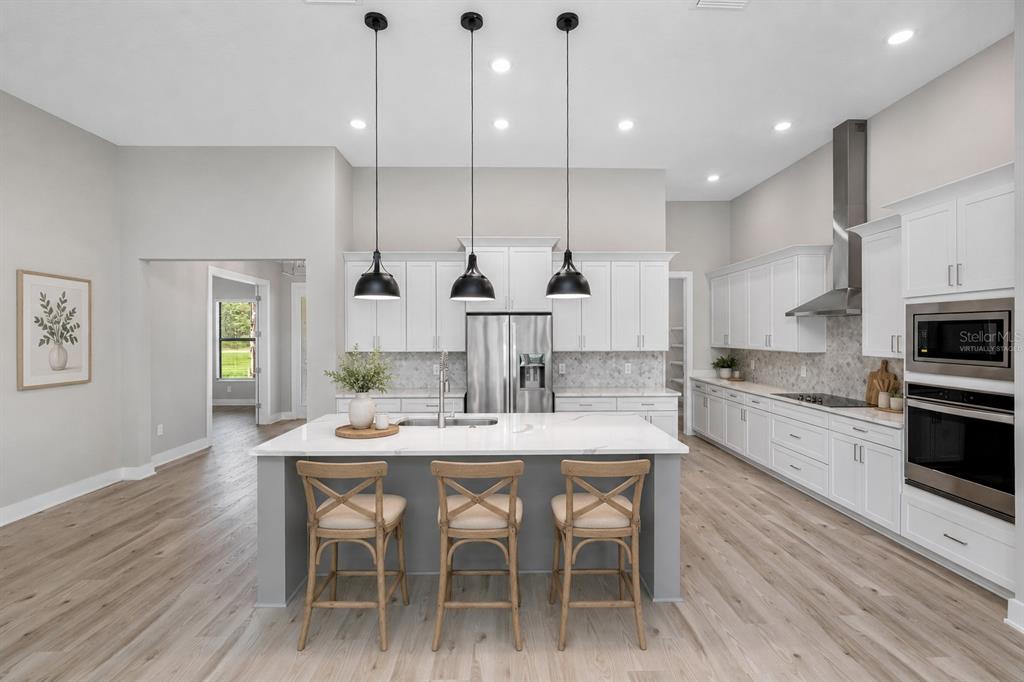 A modern kitchen features white cabinetry, a gray island with three stools, and pendant lighting — 13063 OLDENBURG DRIVE, HUDSON, FL