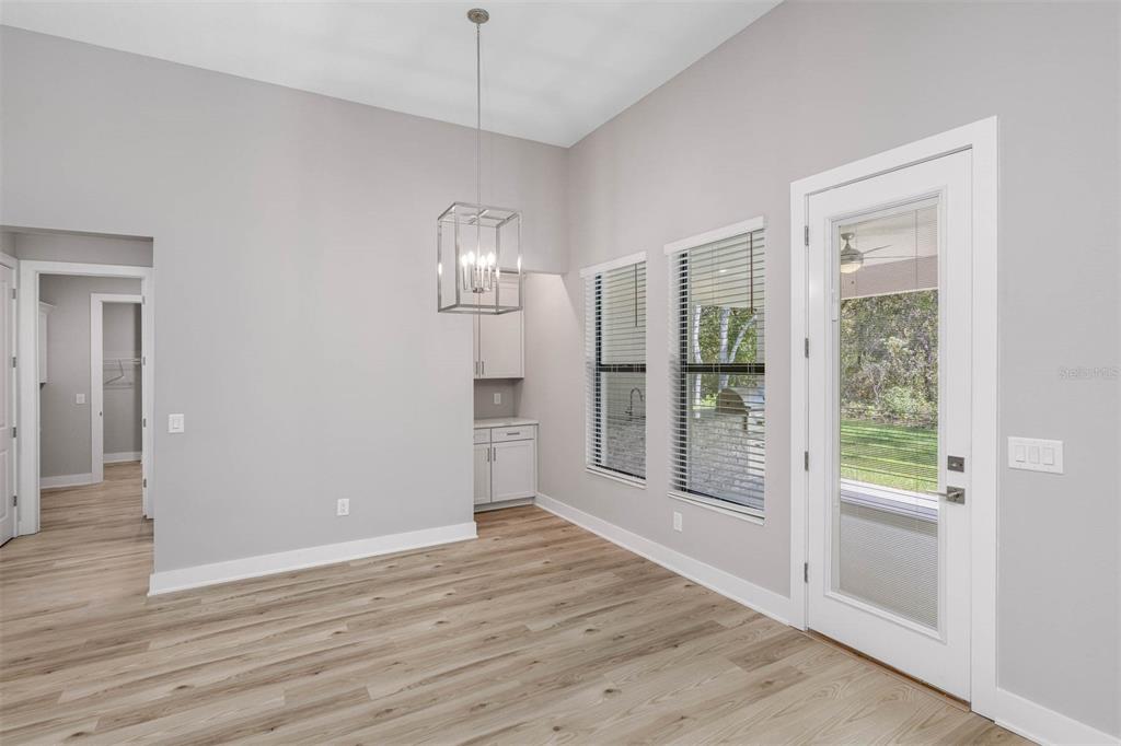 A dining area features light wood-look flooring, a modern chandelier, gray cabinetry, and a glass door — 13063 OLDENBURG DRIVE, HUDSON, FL