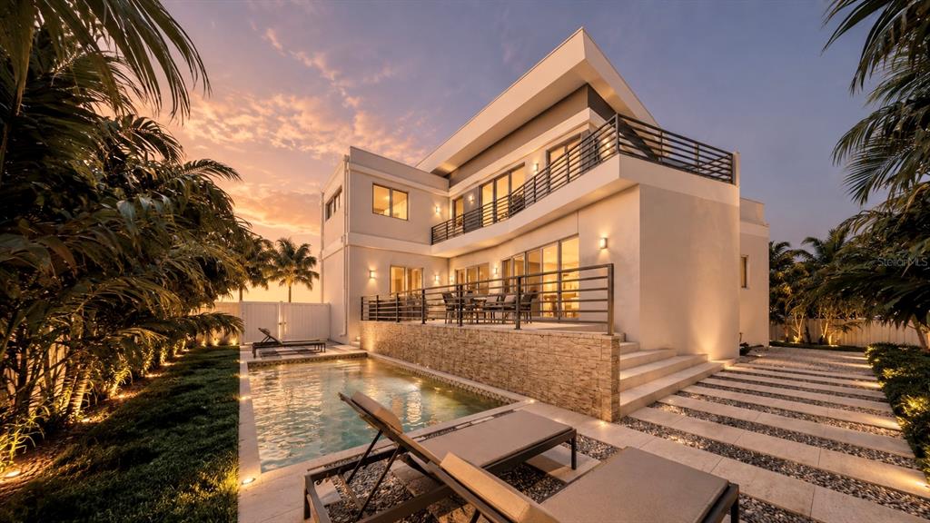 A modern two-story house features a swimming pool, stone patio, and balcony at sunset — 610 HIBISCUS WAY, LONGBOAT KEY, FL