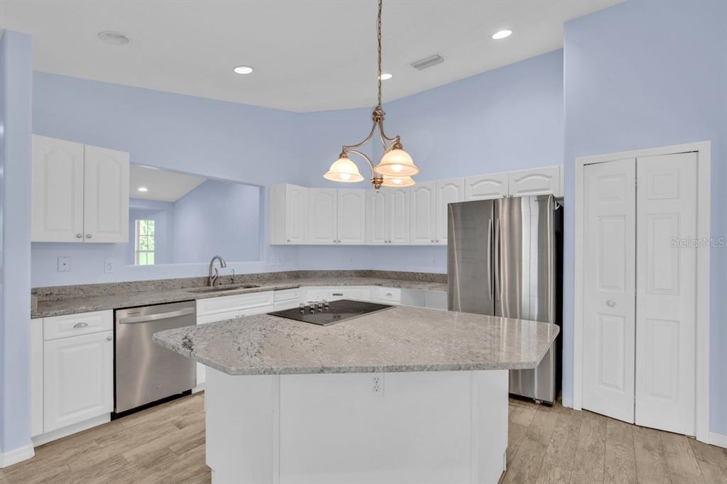 A kitchen features white cabinets, granite countertops, a central island with a cooktop, and stainless appliances — 821 ROBIN LANE, SEBASTIAN, FL