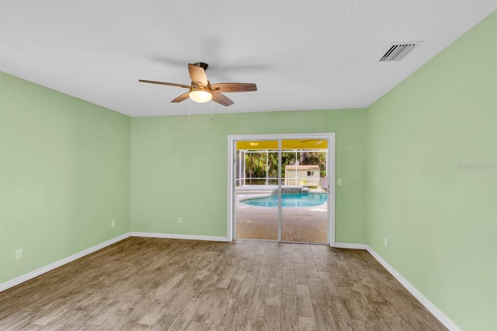 A room with light green walls, wood-look tile flooring, a ceiling fan, and sliding glass doors — 821 ROBIN LANE, SEBASTIAN, FL