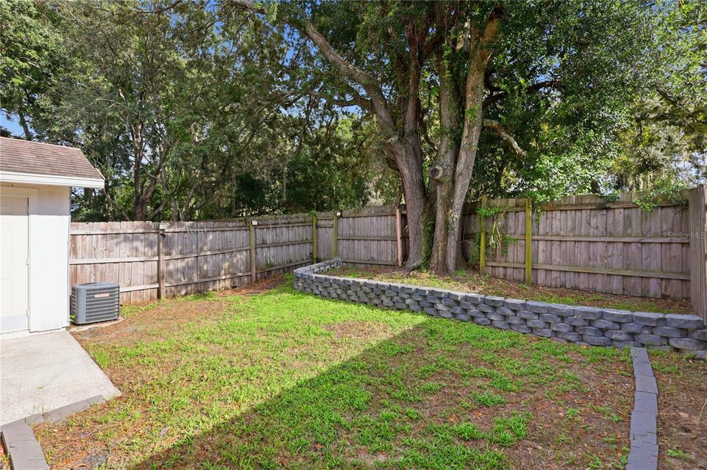A backyard features a concrete patio, a small lawn, a stone retaining wall, and fencing — 4631 N PINE HILLS ROAD UNIT 110, ORLANDO, FL