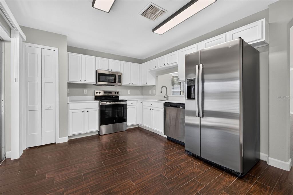 A kitchen with white cabinets, stainless steel appliances, and dark wood-look flooring — 10629 SHADY PRESERVE DRIVE, RIVERVIEW, FL