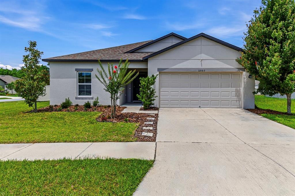 A single-story suburban house with a two-car garage, light-colored stucco exterior, and a manicured lawn — 12103 GOTHIC ROAD, SPRING HILL, FL