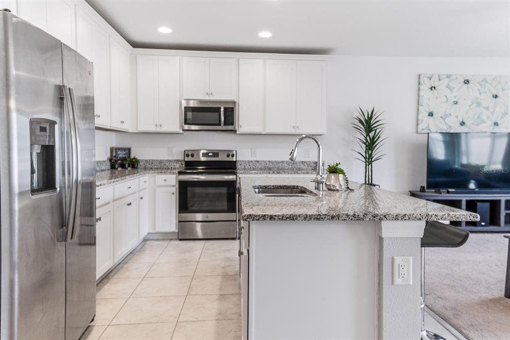 A kitchen features white cabinets, granite countertops, a center island with bar stools, and appliances — 12103 GOTHIC ROAD, SPRING HILL, FL