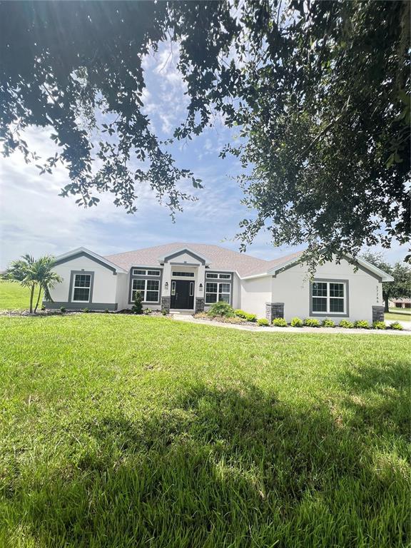 A white single-story house with a gray roof sits on a large, grassy lawn — 37266 HIDDEN VIEW CIRCLE, DADE CITY, FL