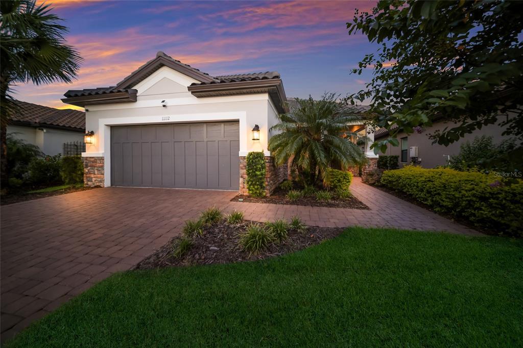 A single-story house with a gray garage door, stone accents, and a brick paver driveway — 11112 DEVONBRIDGE DRIVE, PALMETTO, FL