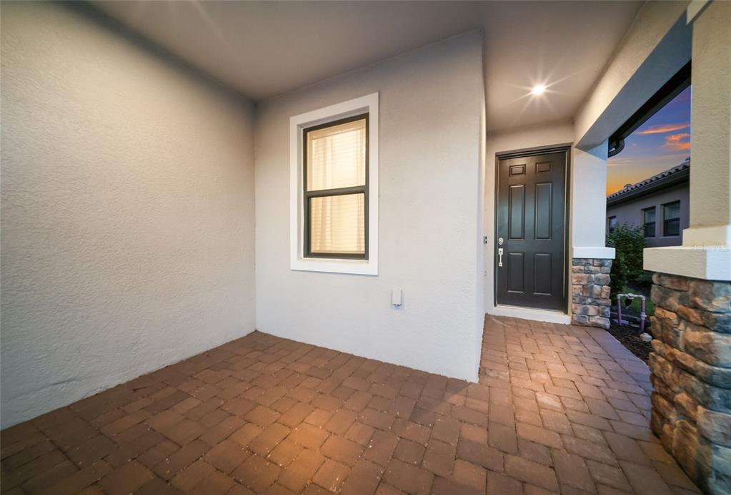 A covered entryway with a brick paver floor, a dark front door, and a window — 11112 DEVONBRIDGE DRIVE, PALMETTO, FL