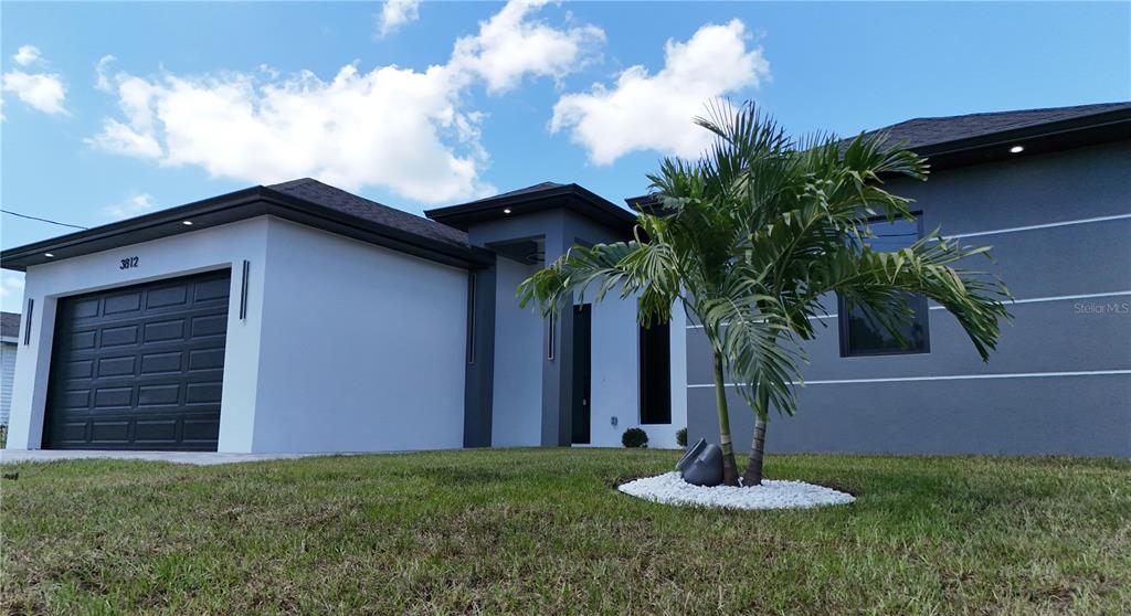 A modern single-story house features a gray and white exterior with a dark garage door — 3812 11TH STREET SW, LEHIGH ACRES, FL