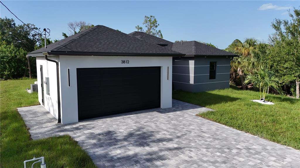 A modern single-story house features a white garage, gray siding, and a paved driveway — 3812 11TH STREET SW, LEHIGH ACRES, FL