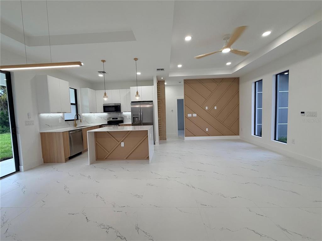 A modern kitchen and living area feature white marble-look tile floors and wood-accented cabinetry — 3812 11TH STREET SW, LEHIGH ACRES, FL