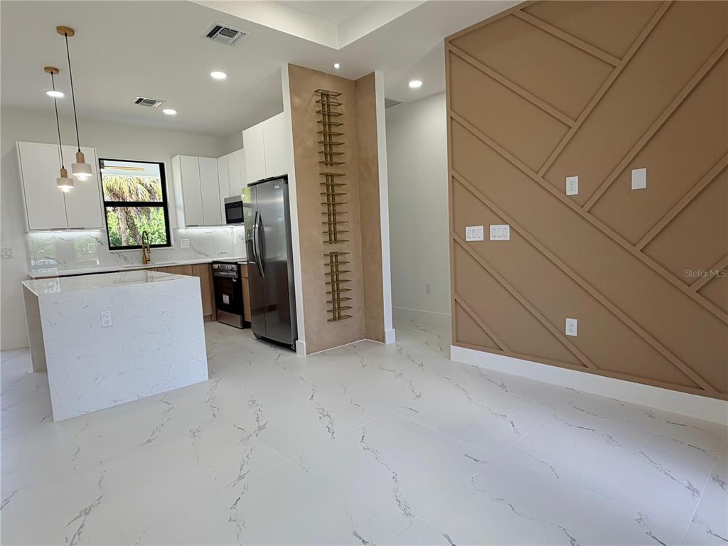 A modern kitchen features white cabinetry, a marble-topped island, and a decorative wood-paneled accent wall — 3812 11TH STREET SW, LEHIGH ACRES, FL