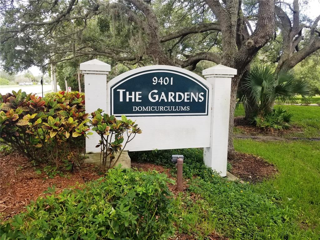 A white monument sign for The Gardens stands in a landscaped area with trees — 8039 GARDEN DRIVE UNIT 109, SEMINOLE, FL