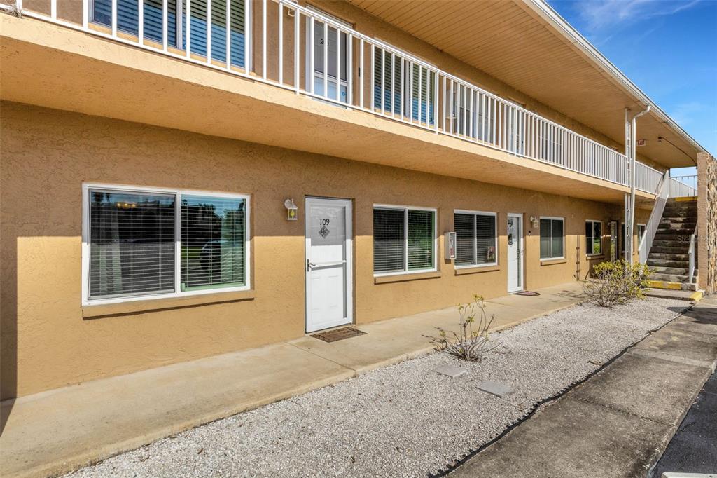 A two-story tan apartment building features a ground-level walkway, white doors, and exterior stairs — 8039 GARDEN DRIVE UNIT 109, SEMINOLE, FL