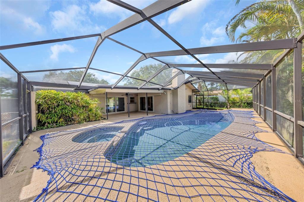 A swimming pool with a safety net is enclosed by a screened lanai behind a house — 3582 FAIRWAY FOREST DRIVE, PALM HARBOR, FL