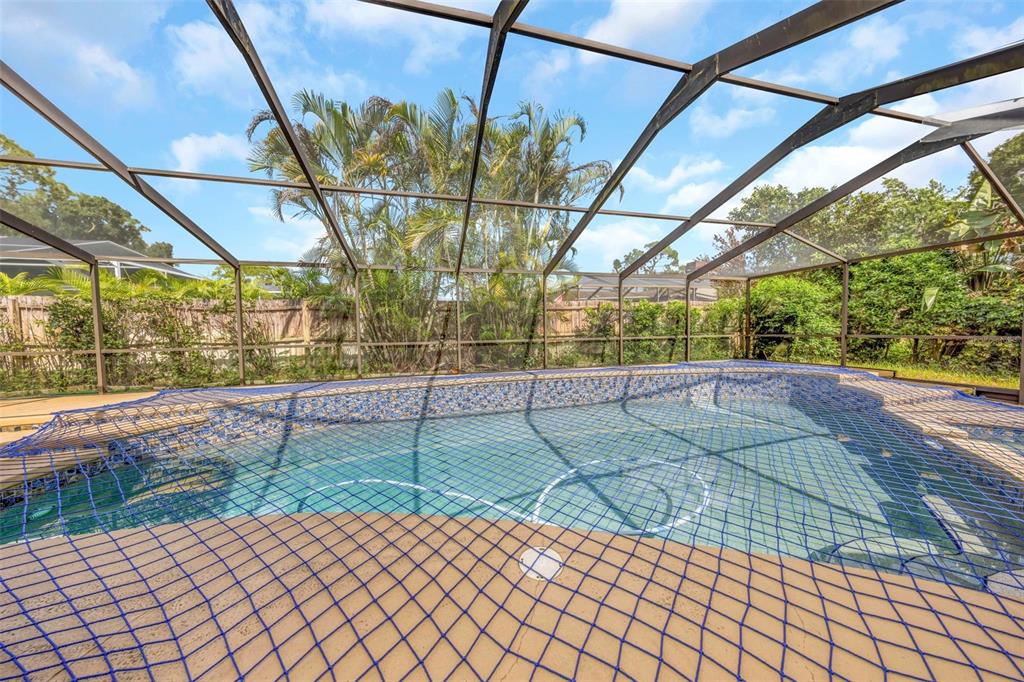 A swimming pool enclosed by a screened lanai features a blue safety net cover — 3582 FAIRWAY FOREST DRIVE, PALM HARBOR, FL