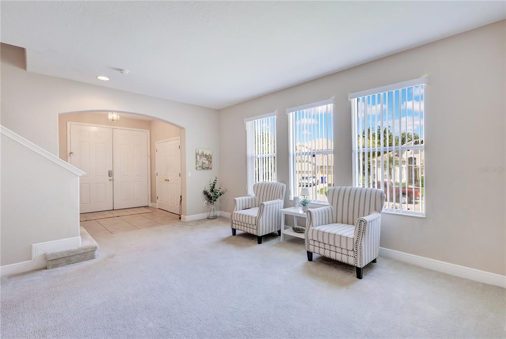A carpeted living area features two striped armchairs, a small side table, and large windows — 1411 PLUMGRASS CIRCLE, OCOEE, FL