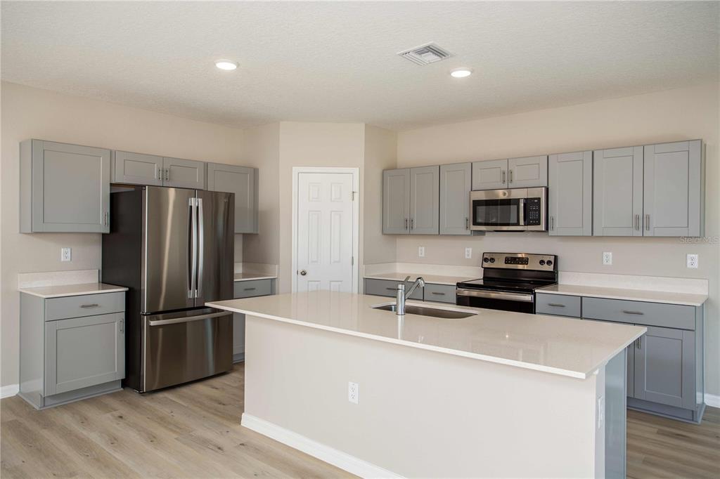 A kitchen features gray shaker cabinets, stainless steel appliances, and a large central island — 9062 BELLEVIEW FOREST PASS, DADE CITY, FL
