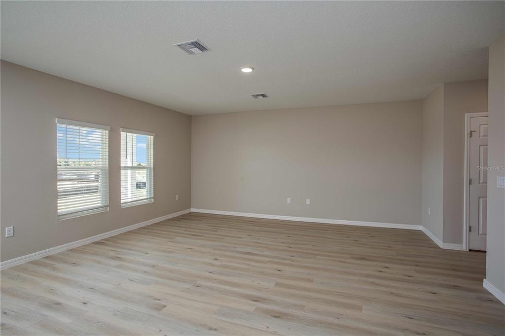 An empty room features light wood-look flooring, beige walls, two windows, and a white door — 9062 BELLEVIEW FOREST PASS, DADE CITY, FL